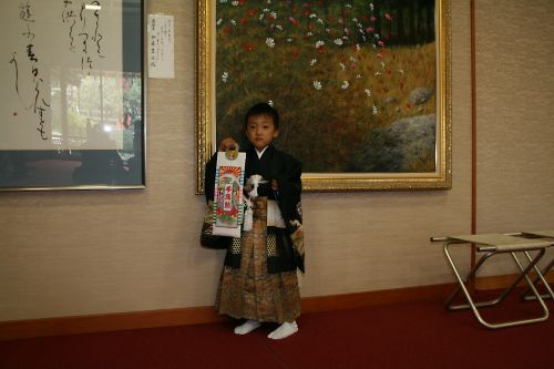 立派に神社の祈祷の間の前で千歳あめを持ってはかま姿で立つKen