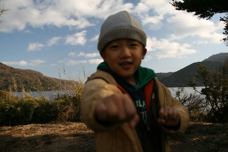 芦ノ湖と空をバックに、正拳突きをしてみせるKen(笑顔)